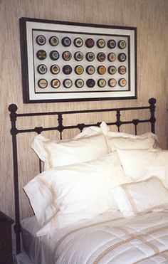 a bed with white sheets and pillows under a framed picture on the wall above it