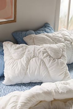 a bed with white and blue pillows on top of it next to a framed painting