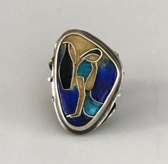 This one of a kind ring depicts a woman seated by a body of water with a jug on her side. The lovely shades of blue, yellow and black enamel go together beautifully. The triangular face is 1" at its longest and 3/4" at its widest. The sides of this ring have five silver bars attaching the face to the shank which is a smooth band. It is marked 800 and Handarbeit (handmade in German). Please note that the silver bars on one side of the ring have at some point been bent. This does not diminish from Unique Blue Enamel Ring, Unique Collectible Enamel Ring, Women Figure, Gold Snake, Charm Rings, Silver Bars, Black Enamel, Turquoise Jewelry, Silver Band