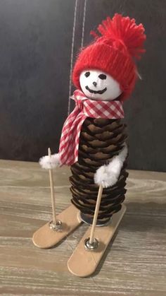 a snowman made out of pine cones with skis attached to the pole and wearing a red hat