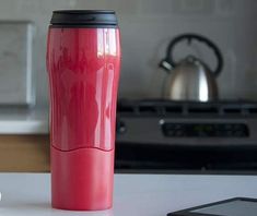 a red coffee cup sitting on top of a white counter next to a cell phone