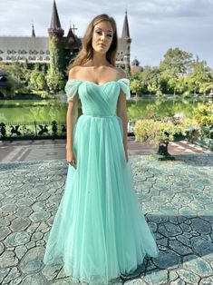 a woman in a blue dress standing on a stone walkway with a castle in the background