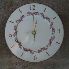 a white clock with gold hands and numbers on the face is shown in front of a carpeted wall