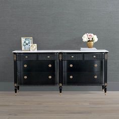 two black dressers with gold handles and white marble top in front of a gray wall