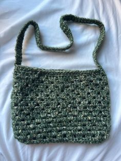 a green crocheted purse sitting on top of a white bed covered in sheets