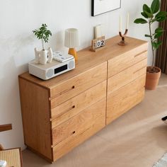 a room with a wooden dresser next to a plant and pictures hanging on the wall