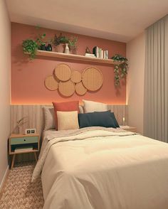 a bed with pillows and blankets in a bedroom next to a wall mounted shelf filled with potted plants