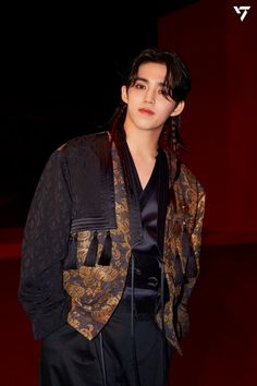 a young man with black hair wearing a jacket and pants, standing in front of a red wall