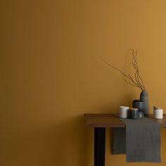 a table topped with vases and candles on top of a wooden table next to a yellow wall