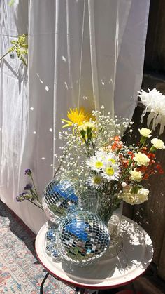 a vase filled with white and yellow flowers on top of a glass table next to a window