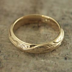 a gold wedding ring sitting on top of a stone floor with an engraved design in the middle