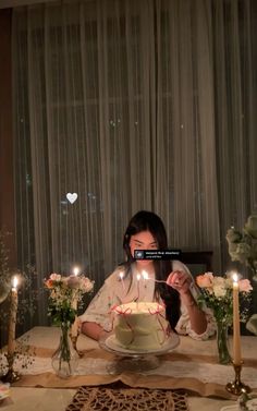 a woman sitting at a table in front of a cake with lit candles on it