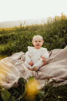 a baby sitting on top of a blanket in the middle of a grass covered field