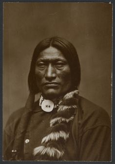 an old photo of a native american man with fur on his head and collar, wearing a