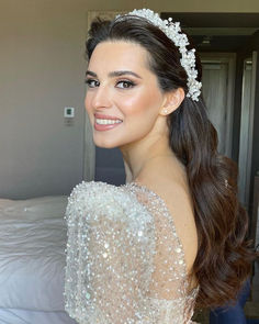 a woman with long hair wearing a tiara and smiling in front of a bed