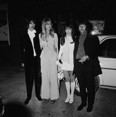 four people standing next to each other in front of a white car at night time