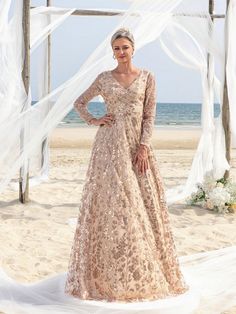 a woman standing on top of a beach next to a white net covered arch with flowers