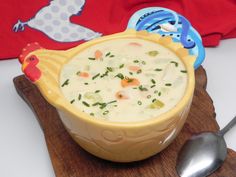 a yellow bowl filled with soup on top of a wooden cutting board next to a spoon