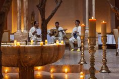 a group of men sitting around a table with candles in front of them and one man playing the guitar