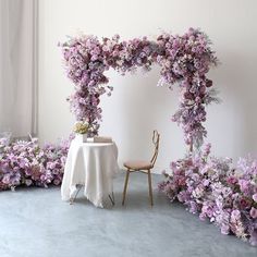 a table with a white cloth and purple flowers on it, next to a chair