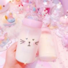 a hand holding a pink cup with a cat face on it and other items in the background