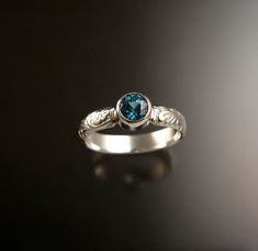 a silver ring with a blue topazte stone in the center on a black surface