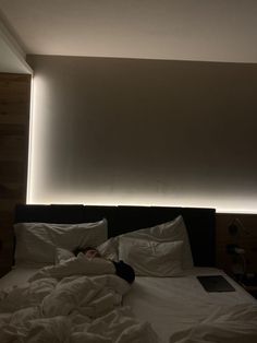 a person is laying in bed with white sheets and blankets on it, under the lights