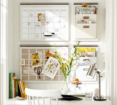 a white desk topped with a vase filled with flowers next to a wall mounted calendar