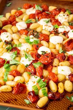 a wooden tray filled with pasta and tomatoes covered in mozzarella sauce, parmesan cheese and fresh basil