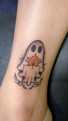 a person with a tattoo on their foot that has a ghost holding an orange leaf