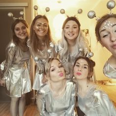 a group of young women standing next to each other in front of a mirror wearing silver dresses