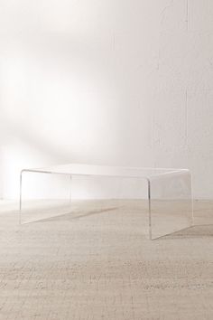 a clear table sitting on top of a wooden floor next to a white brick wall