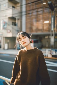 a young woman standing on the street with her hair blowing in the wind and wearing a brown sweater