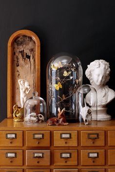 an antique dresser with glass domes and statues on it's top, in front of a black wall