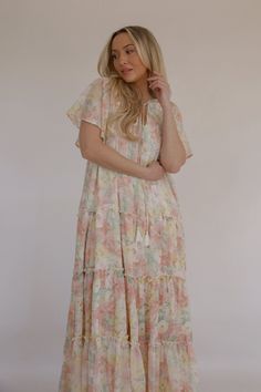 This beautiful Spring Blooms Maxi Dress is perfect for any spring and summer occasion. The flutter sleeves add a feminine touch, while the tiered skirt gives it a flowy, bohemian feel. The stunning floral print adds a pop of color. The maxi length makes it versatile for formal occasions or a casual day out. The lightweight fabric ensures you stay cool and comfortable in warm weather. colors in the dress: pink, white, green and yellow lined relaxed loose fit flutter sleeves smocked top tiered ski Flowy Midi Dress With Ruffle Sleeves For Beach, Summer Flowy Tiered Dress With Ruffle Sleeves, Summer Tiered Dress With Flowy Ruffle Sleeves, Flowy Tiered Dress With Ruffle Sleeves For Summer, Flowy Ruffle Sleeve Tiered Vacation Dress, Vacation Tiered Dress With Ruffle Hem And Flutter Sleeves, Flowy Tiered Dress With Ruffle Hem For Garden Party, Flowy Tiered Dress With Ruffle Sleeves For Vacation, Flowy Floral Dress With Ruffle Hem And Tiered Skirt