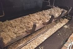 two metal conveyor belts with wood shavings on them