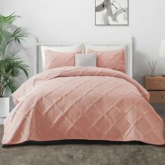 a bed with pink comforter and pillows in a room next to a potted plant