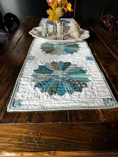 a wooden table topped with a white plate covered in blue and green quilted flowers