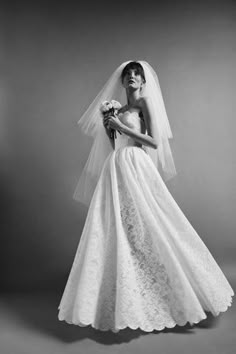 a woman in a wedding dress with a veil on her head and flowers in her hand