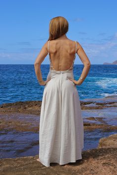 a woman standing on rocks looking out at the ocean with her back to the camera