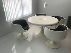 a white table with four black chairs and a round dining room table in the middle