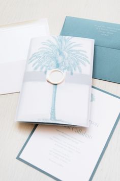 a wedding card with a palm tree on it and a ring resting on the front