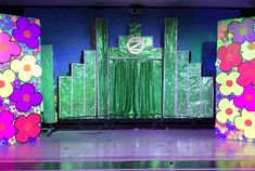 the stage is decorated with colorful flowers and green curtains