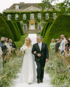 a bride and groom walking down the aisle at their outdoor wedding ceremony in front of an elaborate garden