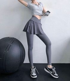 a woman standing next to a black ball wearing grey tights and gray sneakers with her hands on her hips