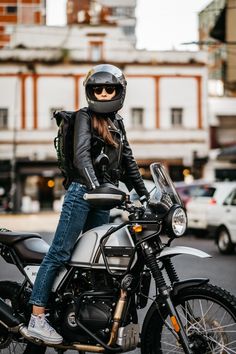 a woman sitting on the back of a motorcycle wearing a black helmet and blue jeans