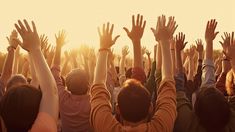 a group of people raising their hands up in the air with sun shining behind them