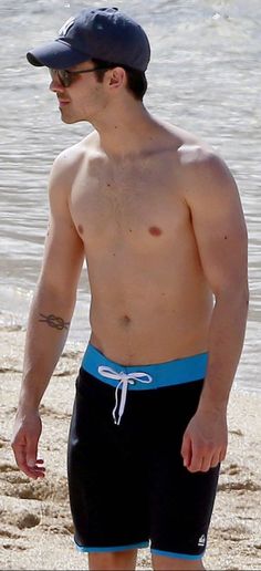 a shirtless man walking on the beach with a frisbee