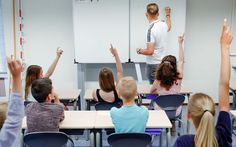 there are many children sitting at desks in front of a man giving a presentation