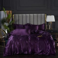 a bed with purple comforter and pillows in a dark room next to a lamp